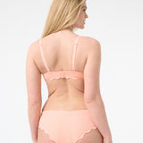 Back of a woman wearing peach colored bikini with scalloped edges