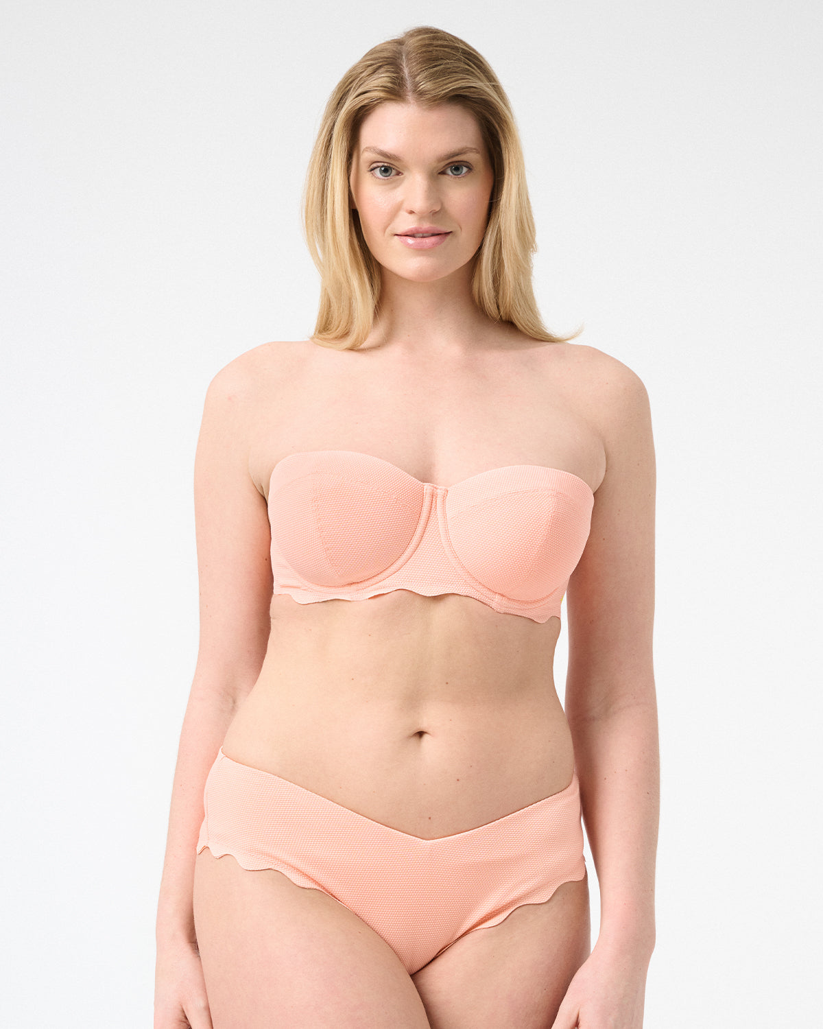 Woman wearing peach colored strapless bikini with scalloped edges