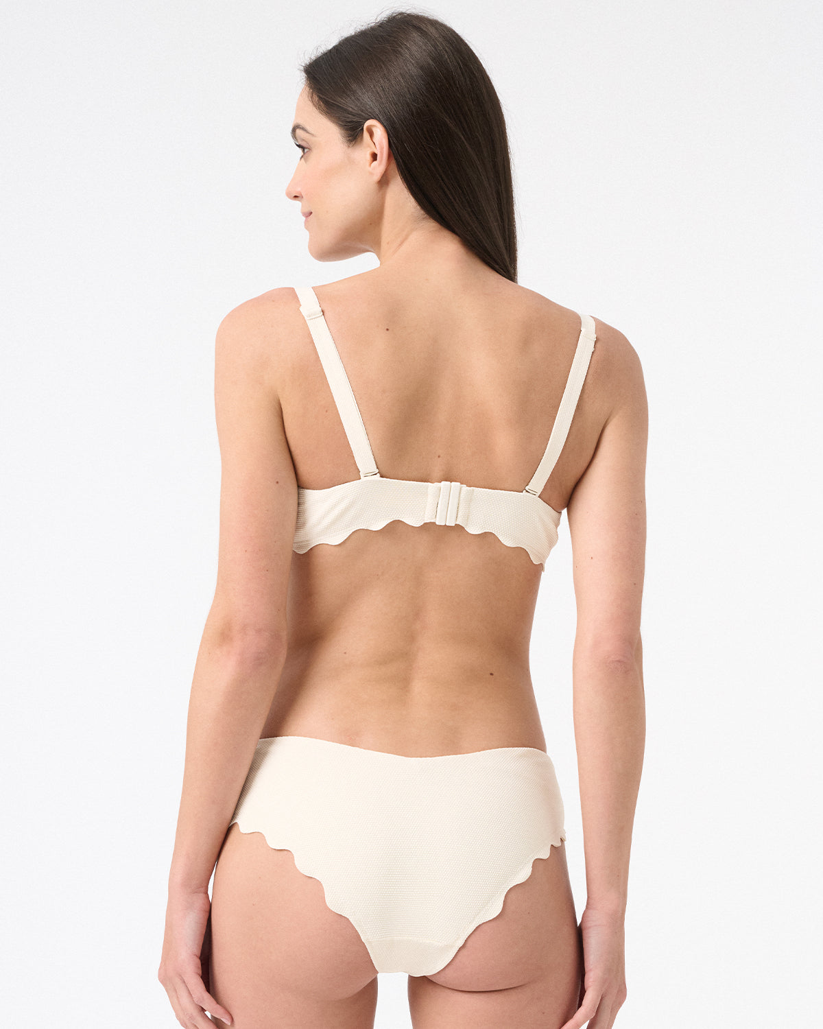 Back view of woman wearing light cream bikini with scalloped edges