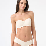 Woman wearing light cream strapless bikini with scalloped edges