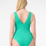 A model is wearing a green one-piece swimsuit with a deep v-neckline and sleeveless design.