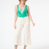 A model is wearing a green one-piece swimsuit with a deep v-neckline and sleeveless design and white long pants and a hat