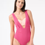 A model is wearing a pink one-piece swimsuit with a deep v-neckline and sleeveless design.
