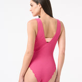 Back of model wearing a pink one-piece swimsuit with a deep v-neckline and sleeveless design.