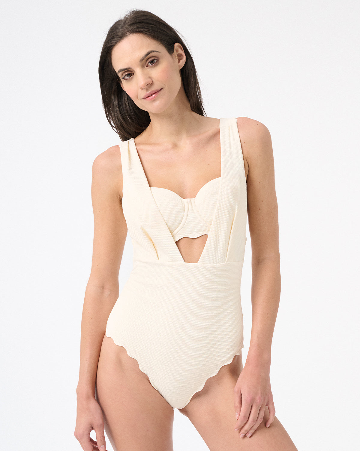 A model is wearing a cream one-piece swimsuit with a deep v-neckline and sleeveless design.