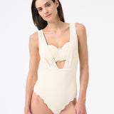 A model is wearing a cream one-piece swimsuit with a deep v-neckline and sleeveless design.