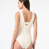 Back of a model wearing a cream one-piece swimsuit with a deep v-neckline and sleeveless design.