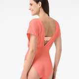 Back of a model wearing a coral one-piece swimsuit with a deep v-neckline and cap sleeve design.