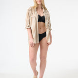 Woman wearing black bikini with a brown and white striped shirt open over top