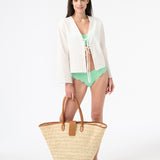 Woman wearing green bikini with a white tie shirt over top while carrying a bag