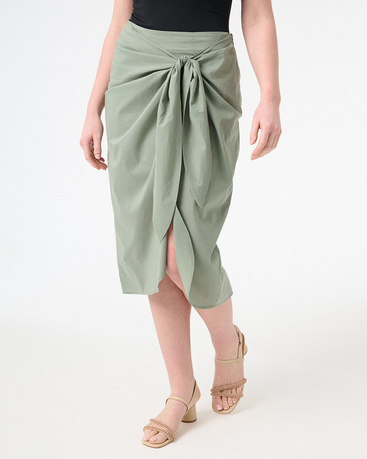 A woman wearing green wrap skirt with black swimsuit underneath