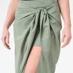 A woman wearing green wrap skirt with black swimsuit underneath