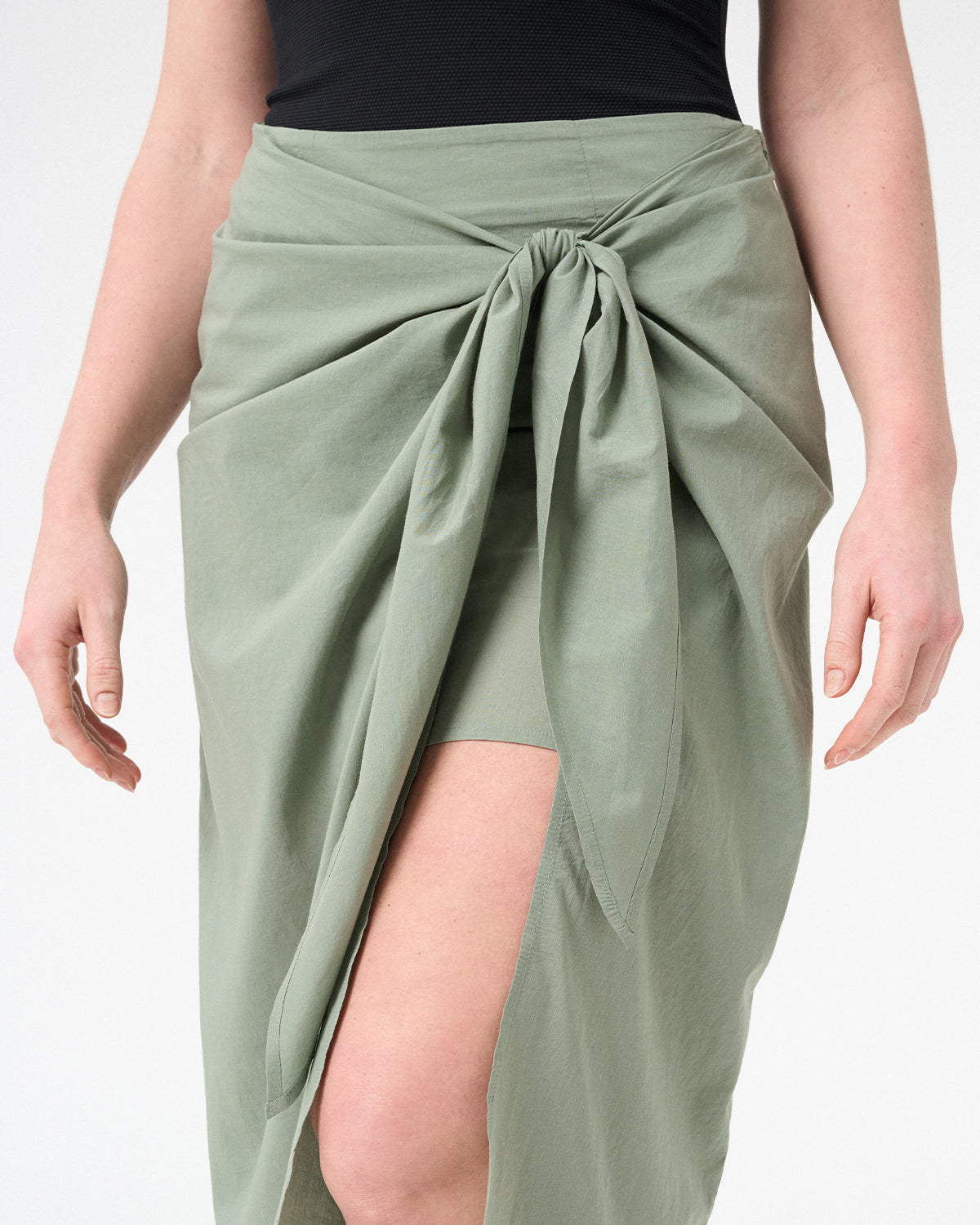 A woman wearing green wrap skirt with black swimsuit underneath