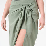 A woman wearing green wrap skirt with black swimsuit underneath
