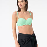 A person wearing a green swim top and a black swim sarong wrapped around the waist.