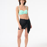 A person wearing a green swim top and a black swim sarong wrapped around the waist.
