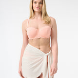 A person wearing a peach swim top and a white swim sarong wrapped around the waist.