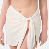 A person wearing a peach swim top and a white swim sarong wrapped around the waist.