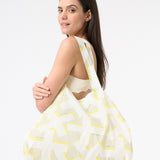 A woman is shown carrying a white and green geometric patterned tote bag over her shoulder.