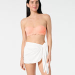 Woman wearing a peach strapless top and white sarong on a white background