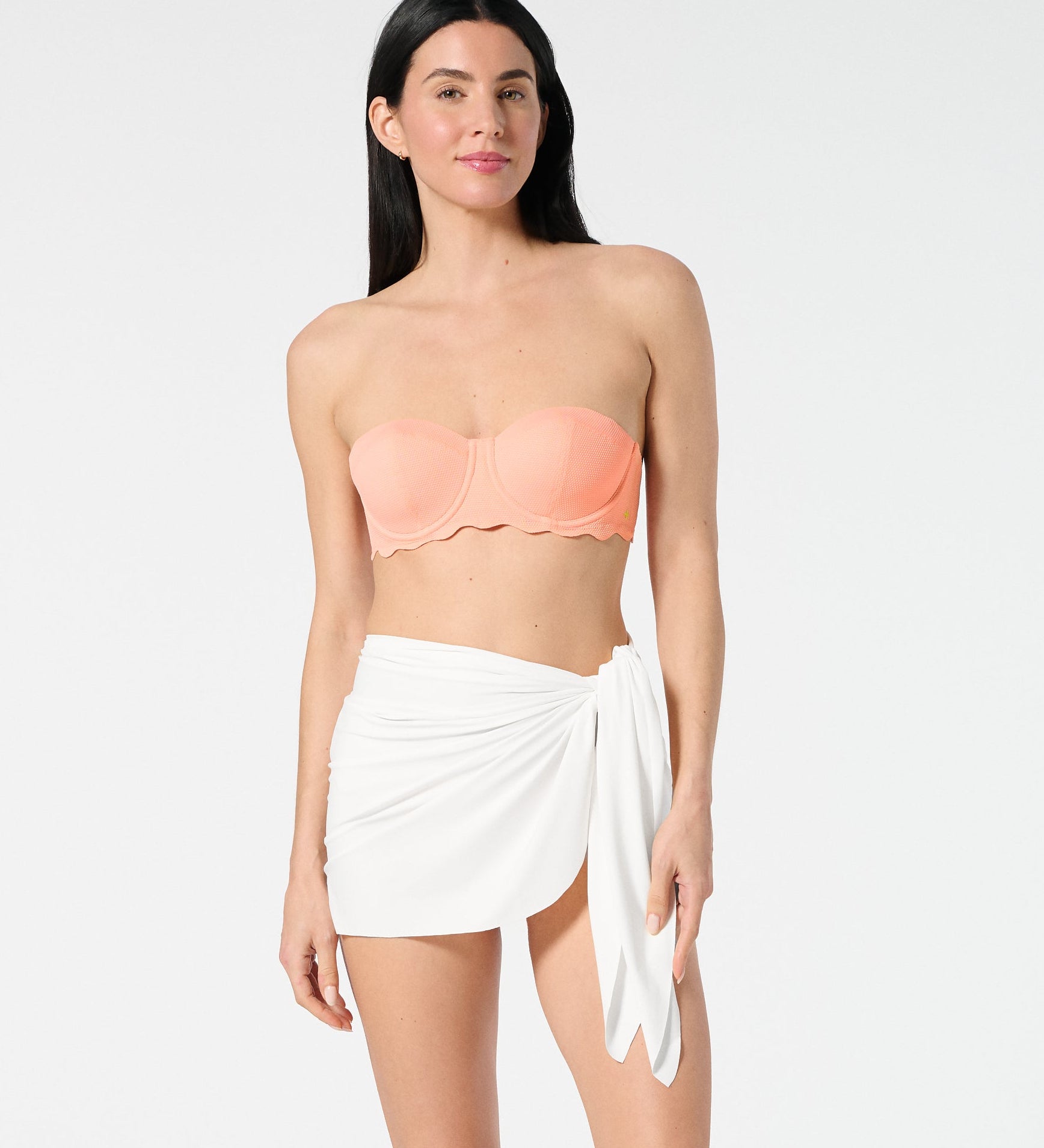 Woman wearing a peach strapless top and white sarong on a white background