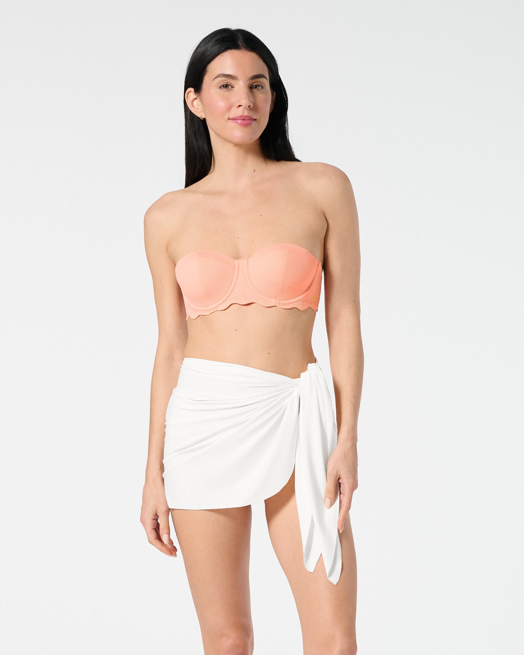 Woman wearing a peach strapless top and white sarong on a white background